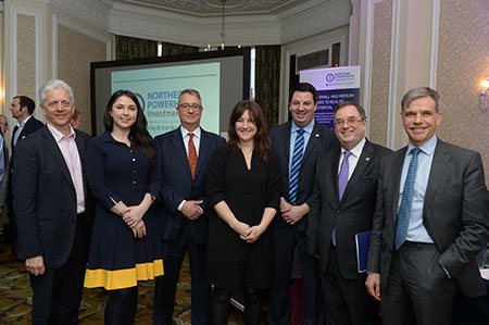 Five men and two women in a row standing in an impressive building at a function.