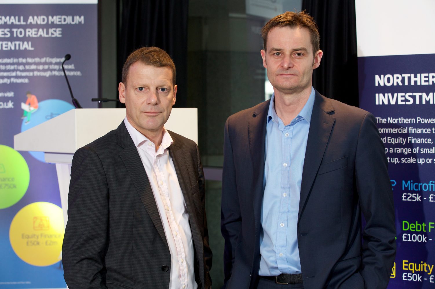 Two businessmen standing next to each other with Northern Investment point of sale behind them.