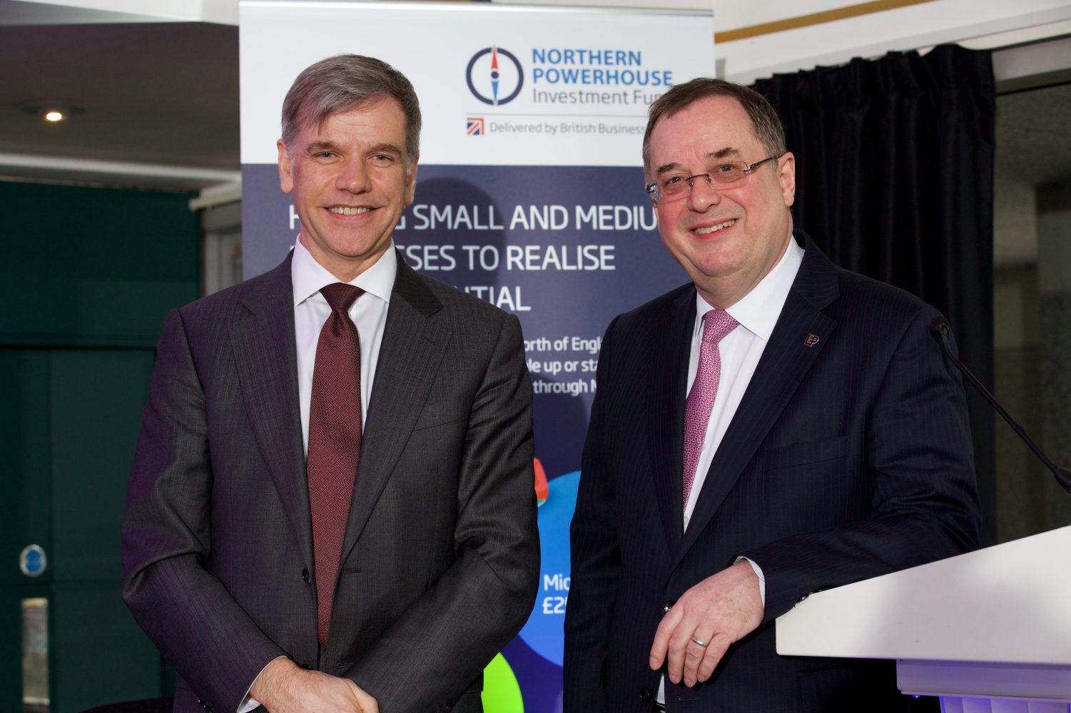 Two men wearing business suits standing in front of Northern Powerhouse point of sale.