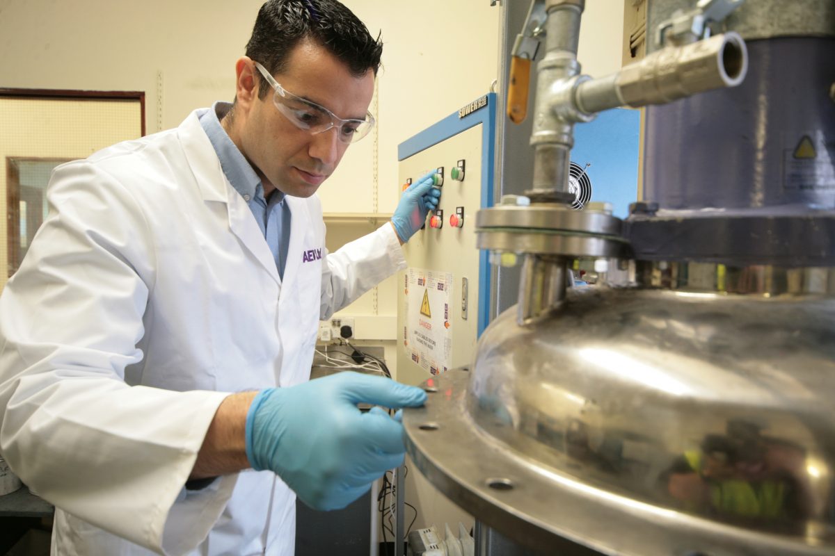 A man in lab coat and safety goggles operating machinery