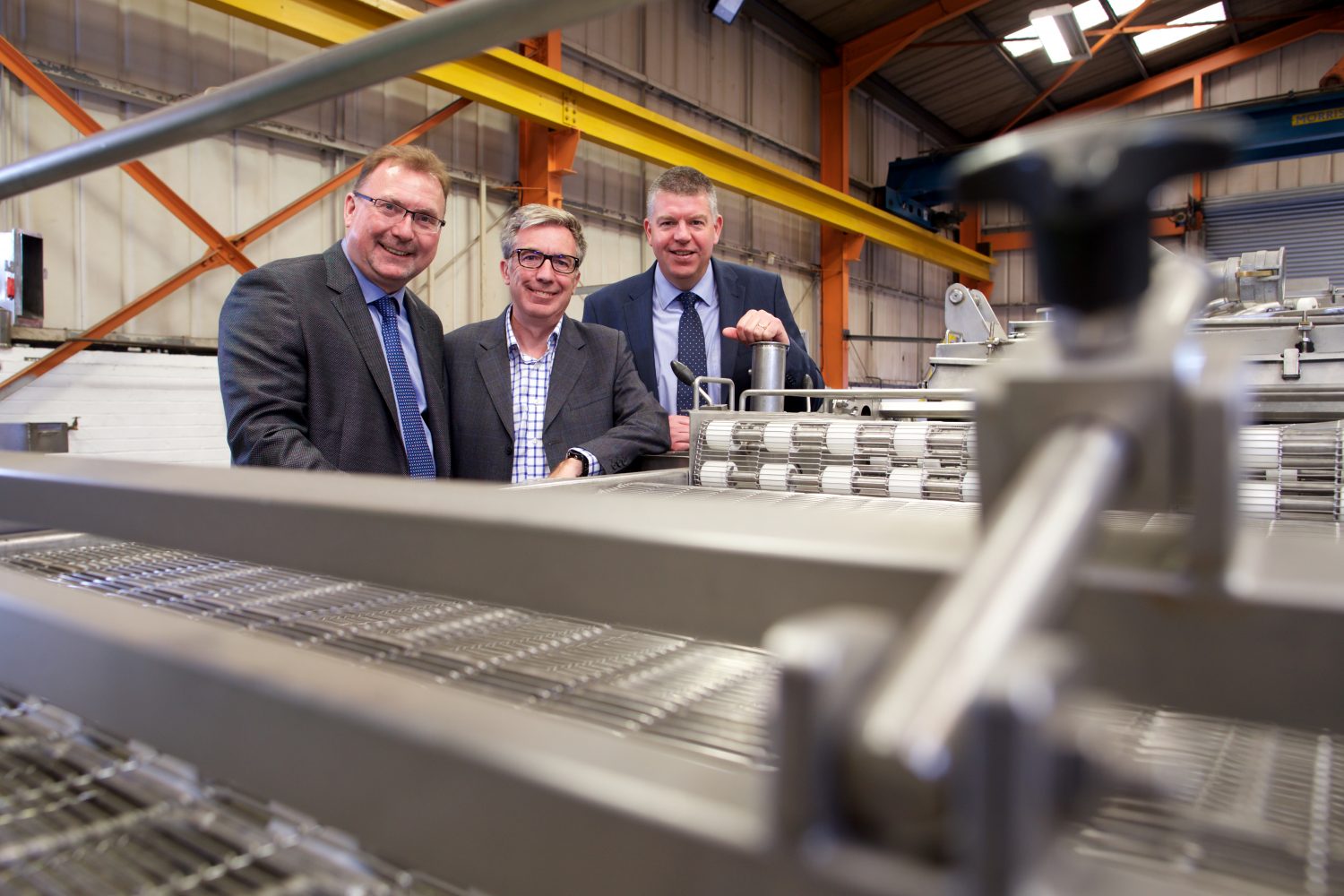 Three men in an industrial setting standing next to equipment.