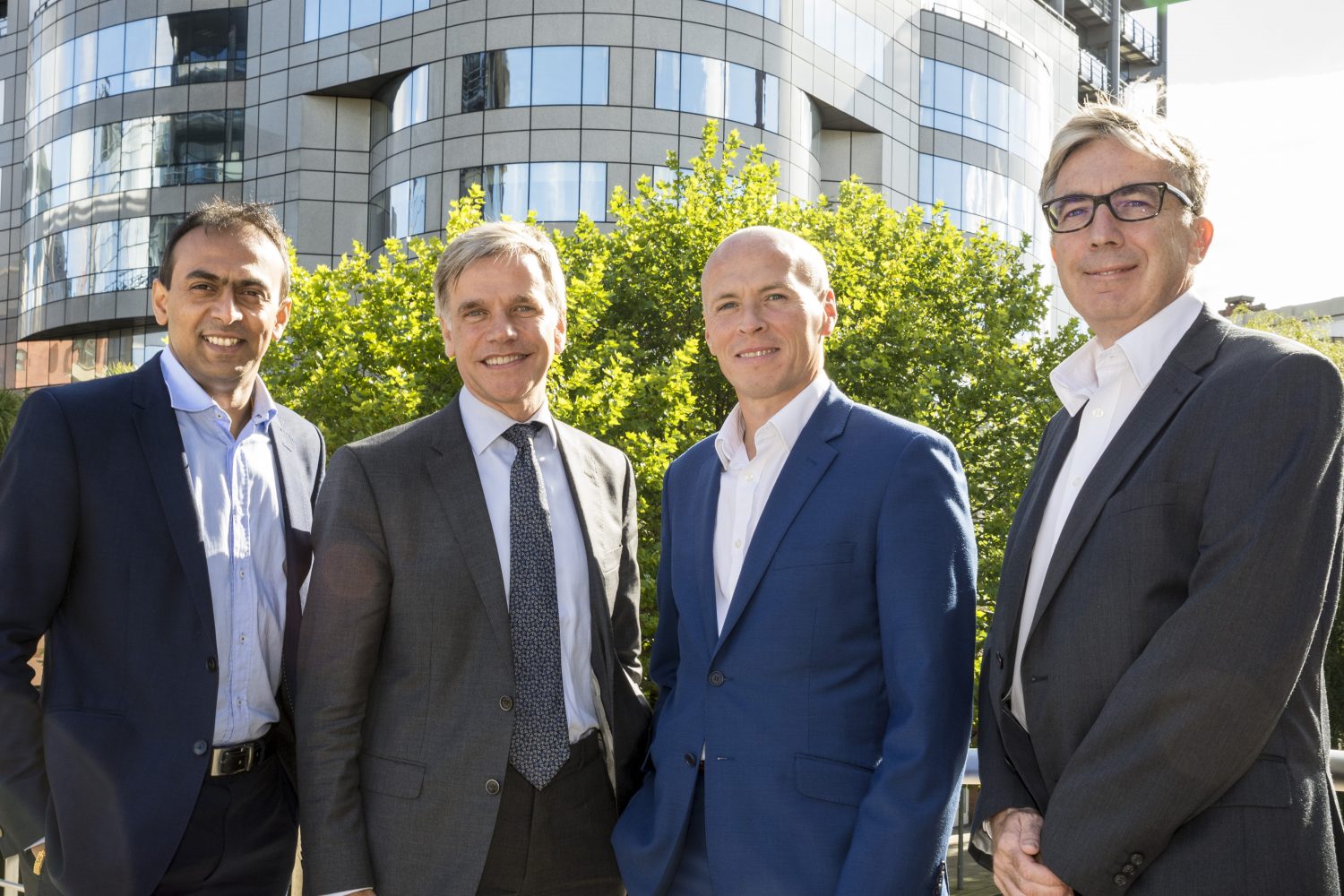 Four businessmen standing in a row outside an office.