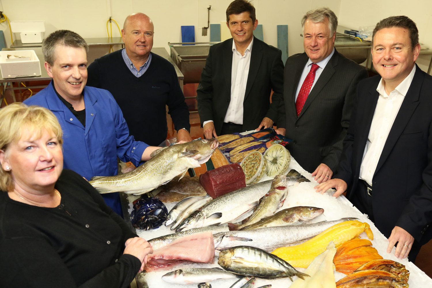 5 men and a woman gathered around a table of fresh fish