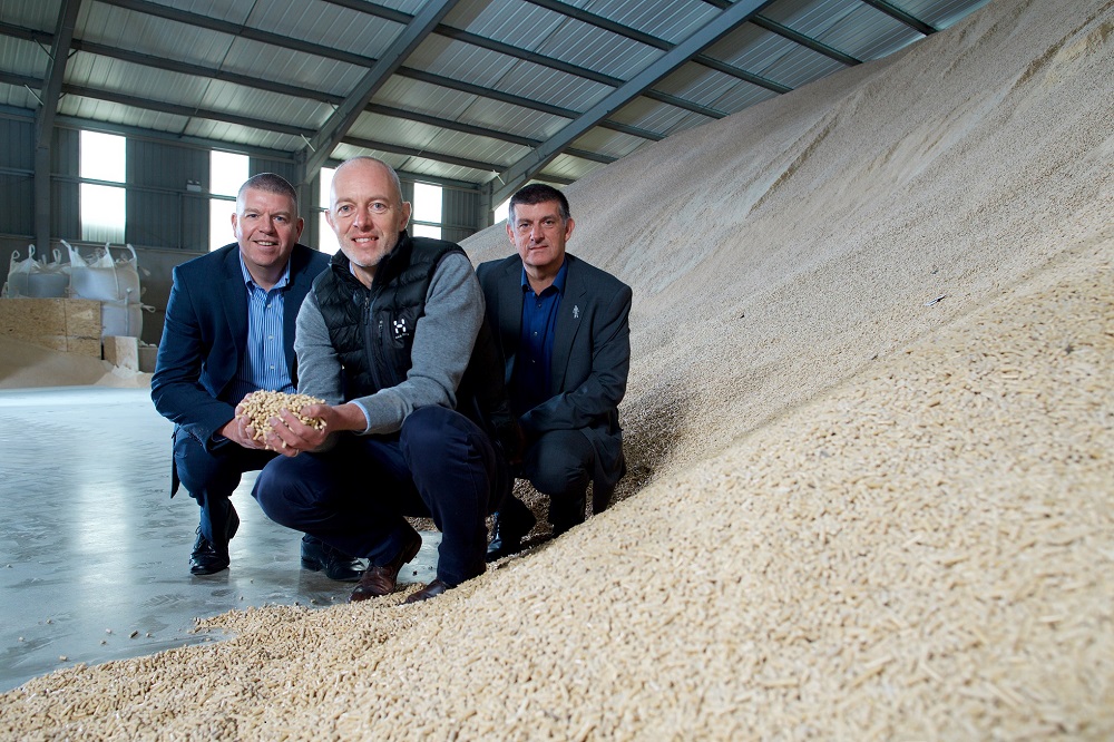 Three men in factory and one man is holding pellets.