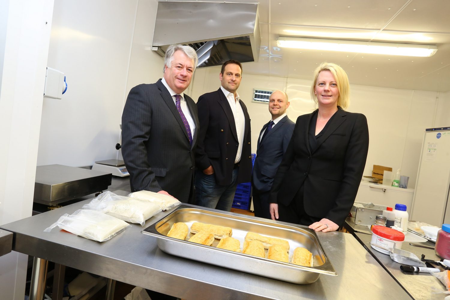 Three businessmen and a business woman standing in an industrial kitchen.