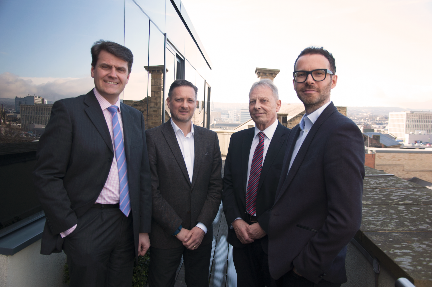 Four suited men standing outside an office building. One man is leaning against the office window.