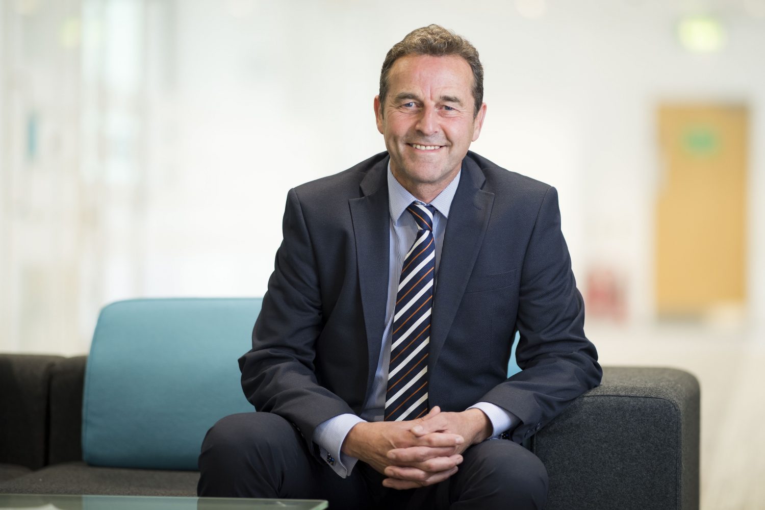 Businessman sitting on a grey sofa with a blue cushion behind him.