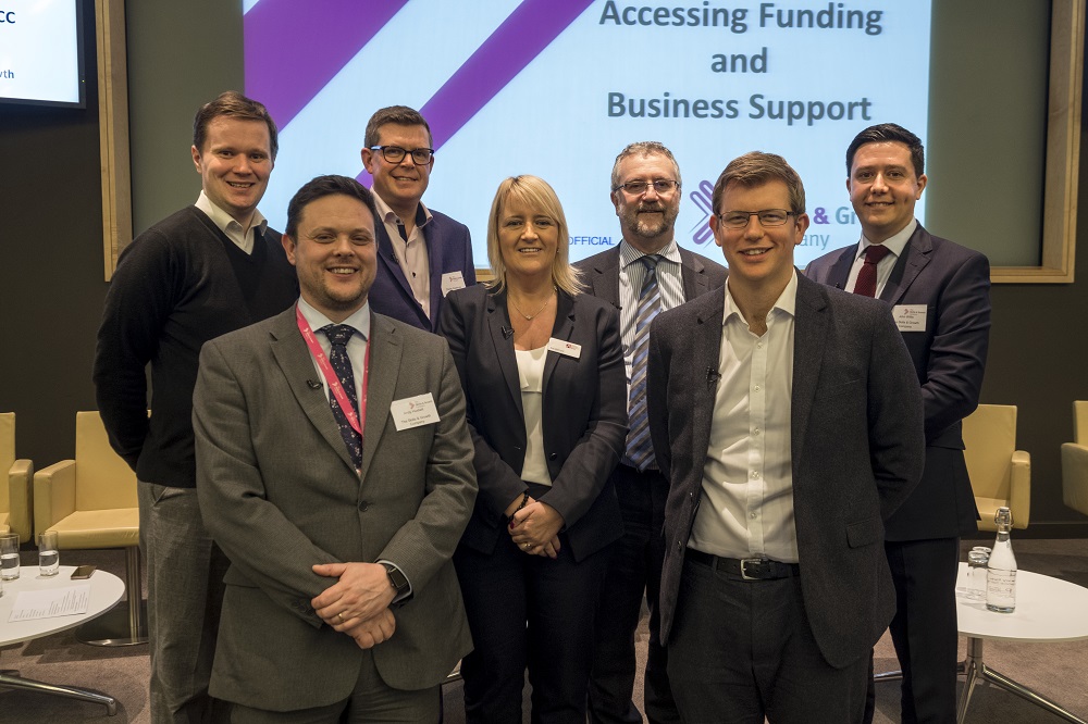 Seven people in a group standing in front of signage stating Accessing Funding and Business Support. There is one woman in the group.