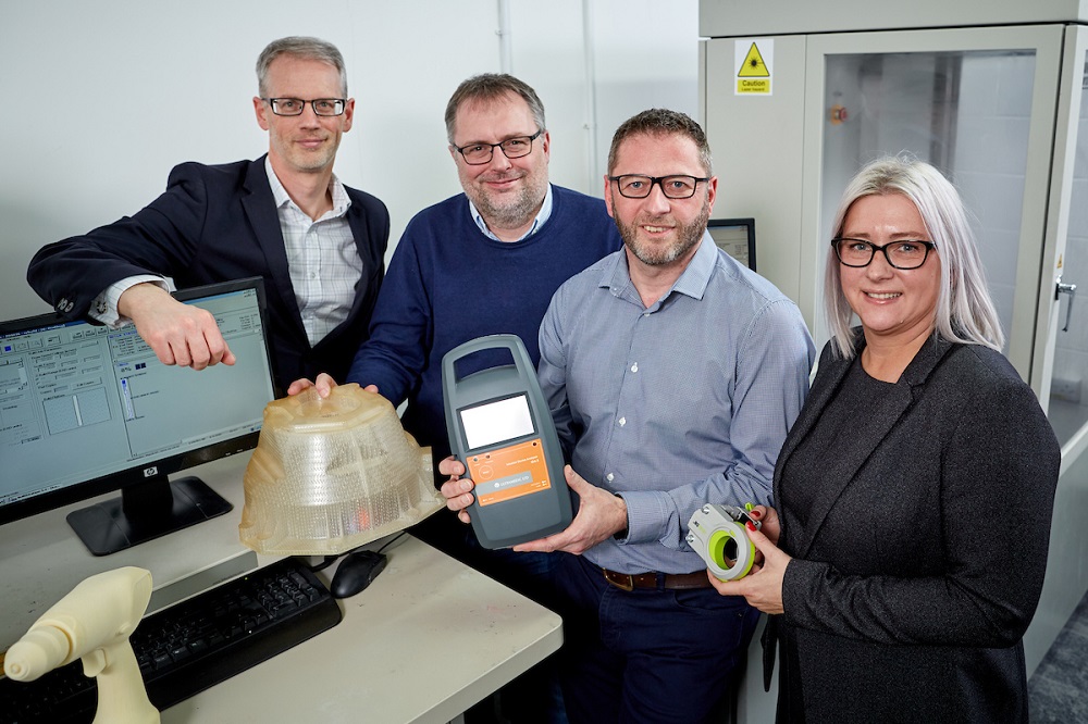 One businesswoman holding industrial product and standing next to her there are three men in an industrial setting. Two of the men are holding some industrial products.