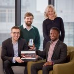 3 men and a woman sat in an office holding smart devices