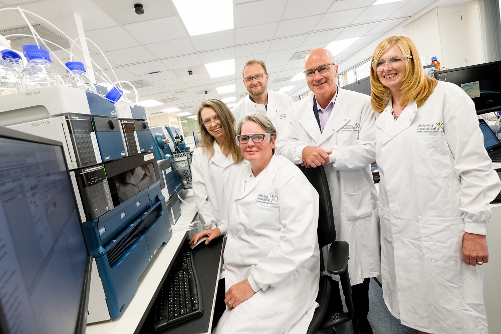 Three women wearing lab coats and two men wearing lab coats located in a laboratory.