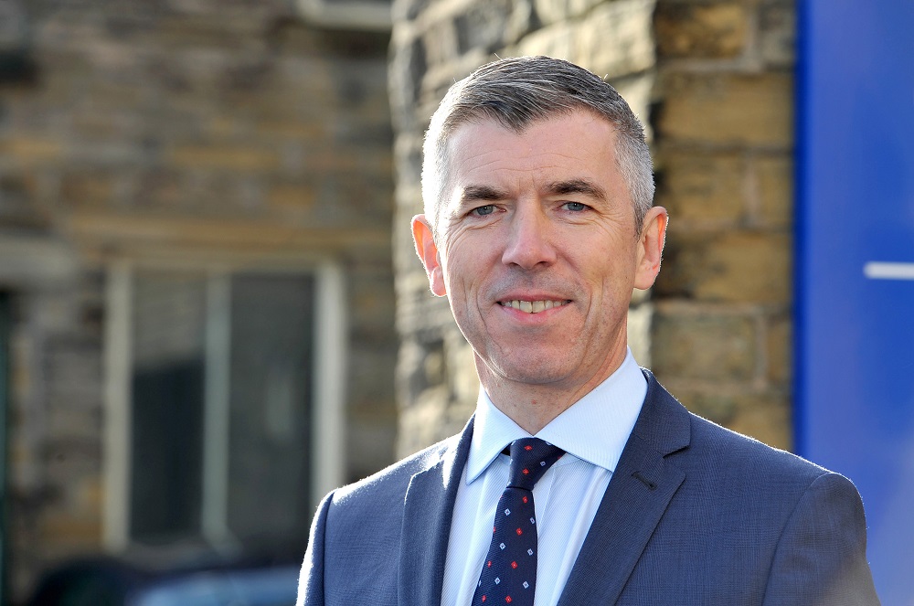 Headshot of David Wright outside a building with grey hair and wearing a blue suit.