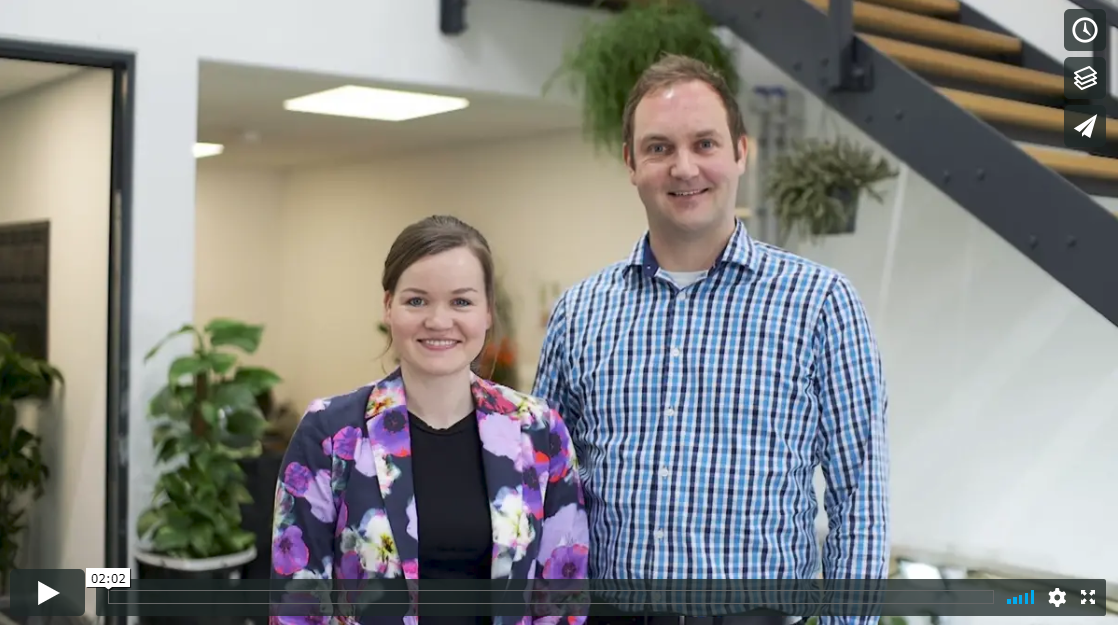 A woman wearing flowery jacket and man wearing checked shirt in an office.