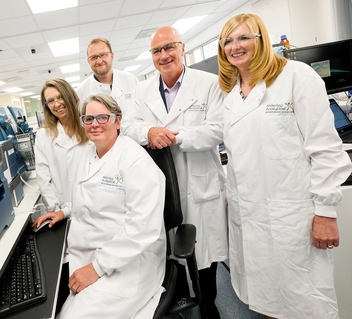 Three women wearing white lab coats and two men wearing white lab coats.