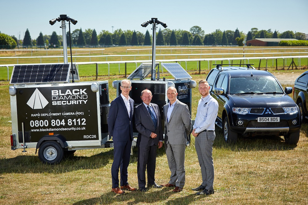 Four men outside in a race course standing in front of 4 wheel drive car .