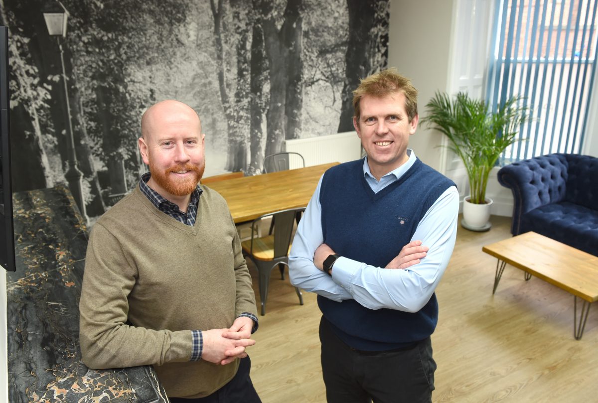 Two men in office, man to the right wearing a blue jerkin and other man is bald with a ginger beard.