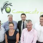 Employees from Communicate Technology smiling and stood in front of a Communicate plc branded wall