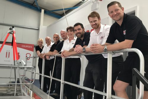 Group of people standing on a platform in an industrial setting. They are all wearing either black or black and white outfits.