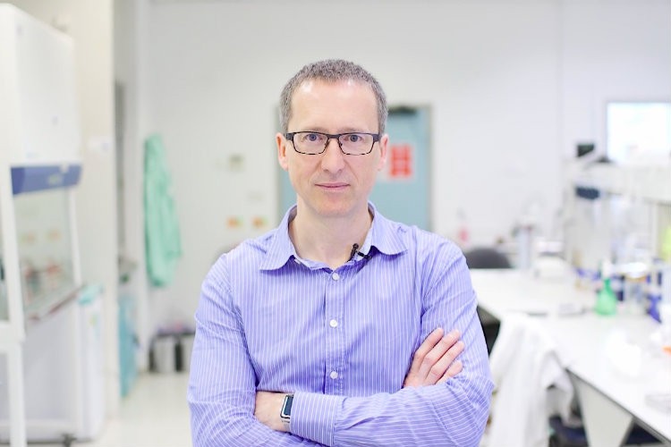 Man with glasses in a laboratory wearing a purple shirt.