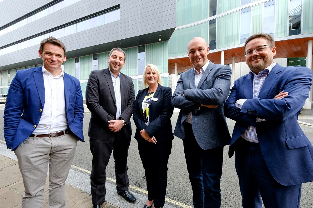 4 men and a woman stood outside of an office building smiling