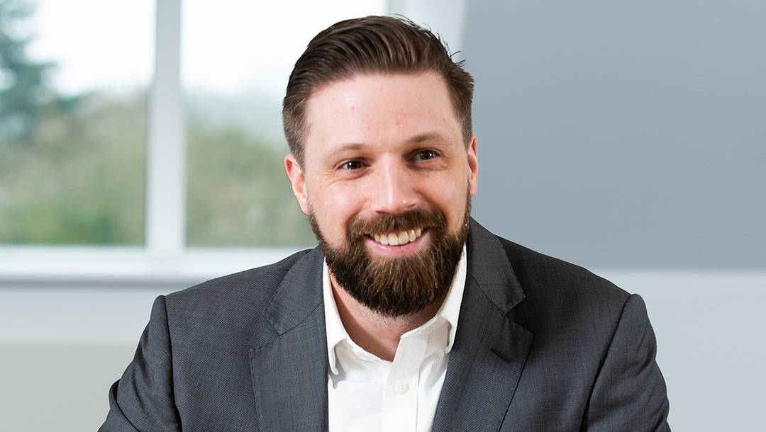 Head shot of Will Schaffer. He has a beard and is wearing a grey suit jacket and cream shirt.