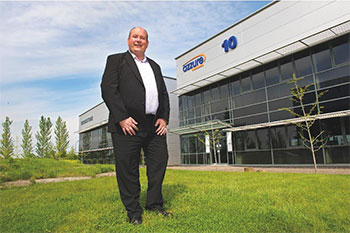 Portly man wearing black suit standing on grass outside office building.