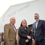 One man to the left wearing a beige suit, woman in the middle wearing black jacket and man to the left wearing a black suit outside Rosehill Polymers factory.