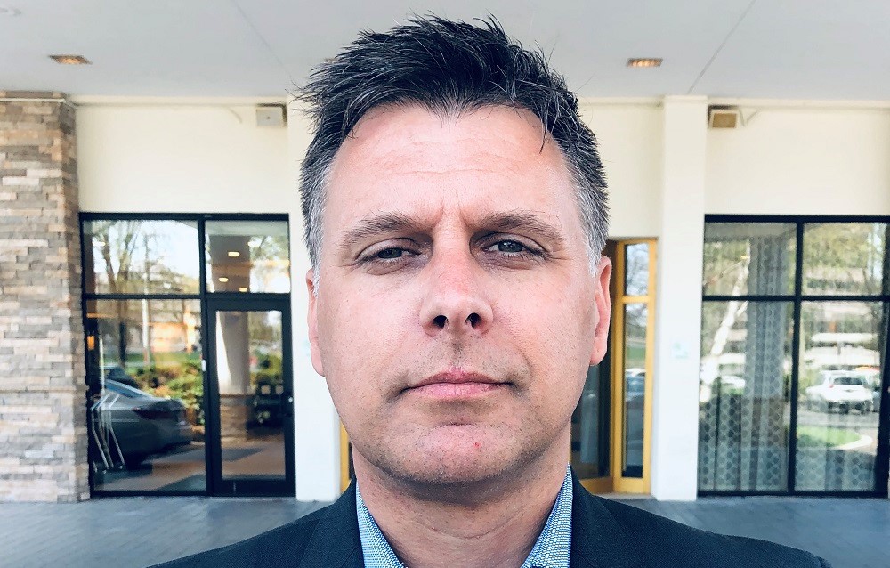 Headshot of Darren Fowler standing in front of building. There is a yellow framed door open in the background.