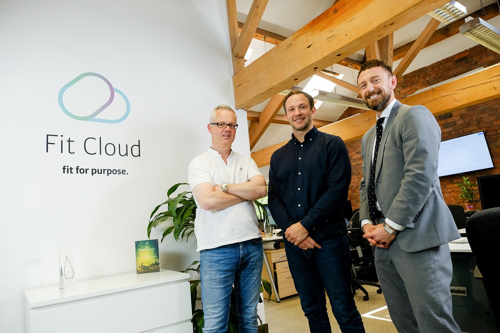 Three men in an office standing next to wooden pillars.