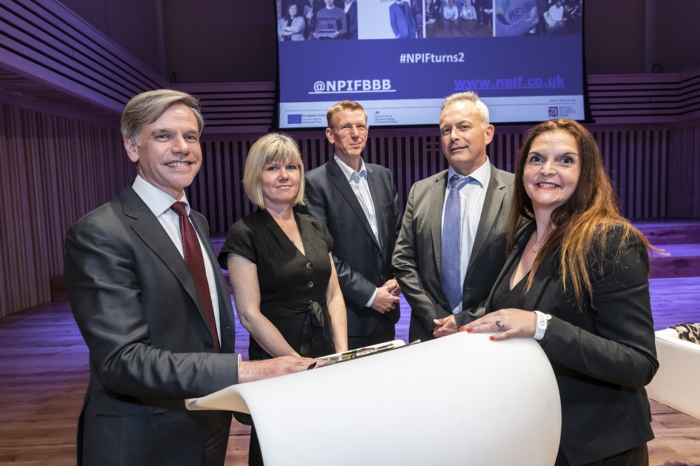 Five people standing around a podium. There are two ladies in the group wearing black outfits and the three men are wearing suits.