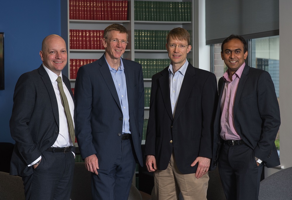 Four suited men standing in front of bookshelves.