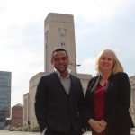 A man and a woman stood outside smiling with building in the background