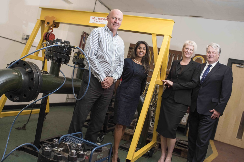 Two woman and two men in a building. One man and woman is standing within a piece of yellow metal equipment.