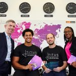 Three men and a woman standing in front a picture of the world map and four clocks.