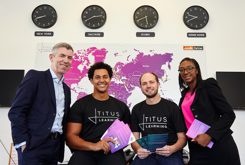 Three men and a woman standing in front a picture of the world map and four clocks.