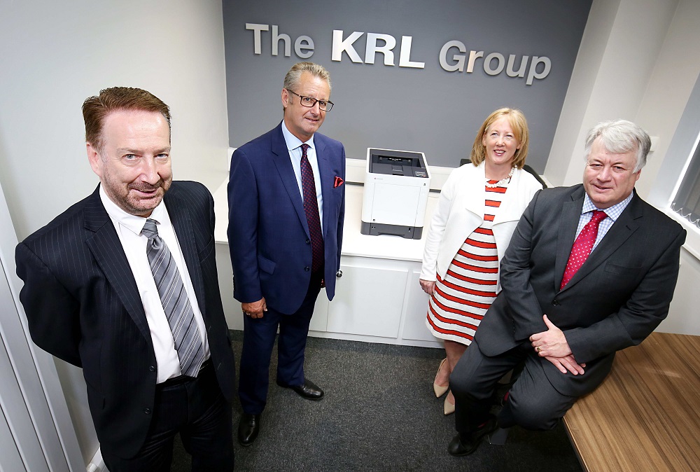 3 men and a woman stood in a small meeting room with The KRL Group sign on the wall in the background