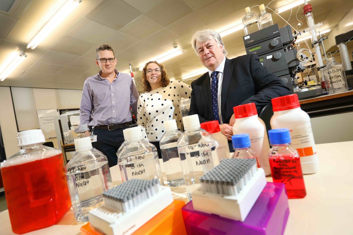 2 men and a woman sat in a science lab with chemicals on the table in front of them