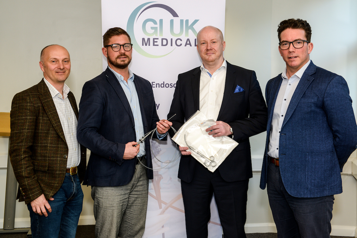 Four men standing in front of GI UK Medical point of sale. Man to right wearing blue jacket, black trousers, white shirt and has glasses on and man to the left hand end is wearing jeans, brown checked jacket