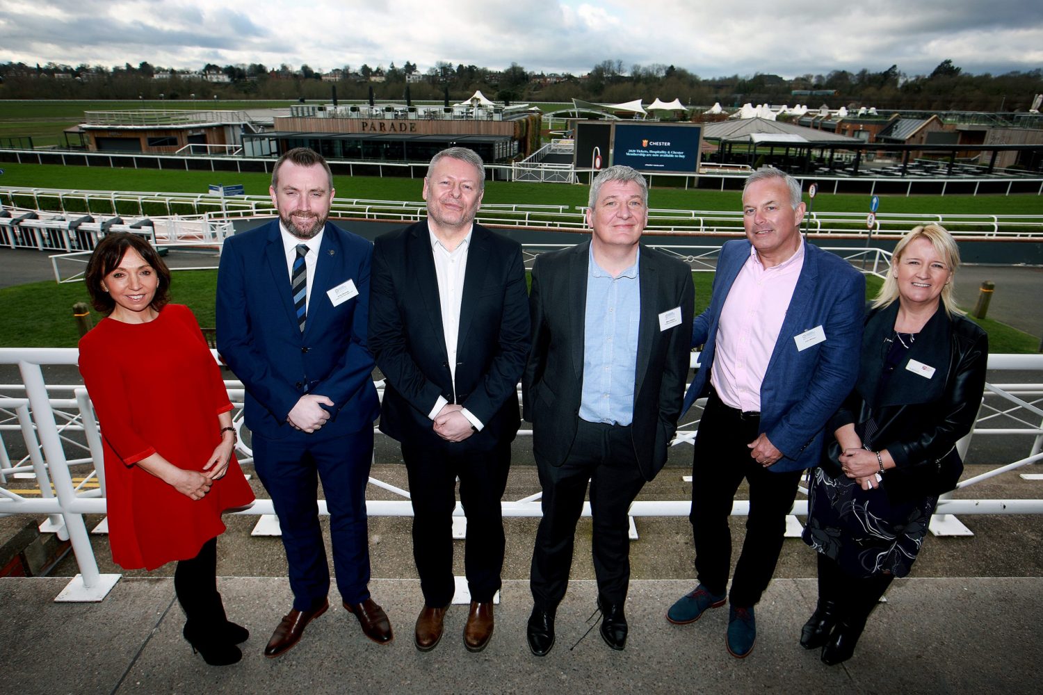 Six people standing in front of horse race trac - two women at the end and four men in the middle