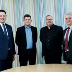 4 men in suits stood in a meeting room