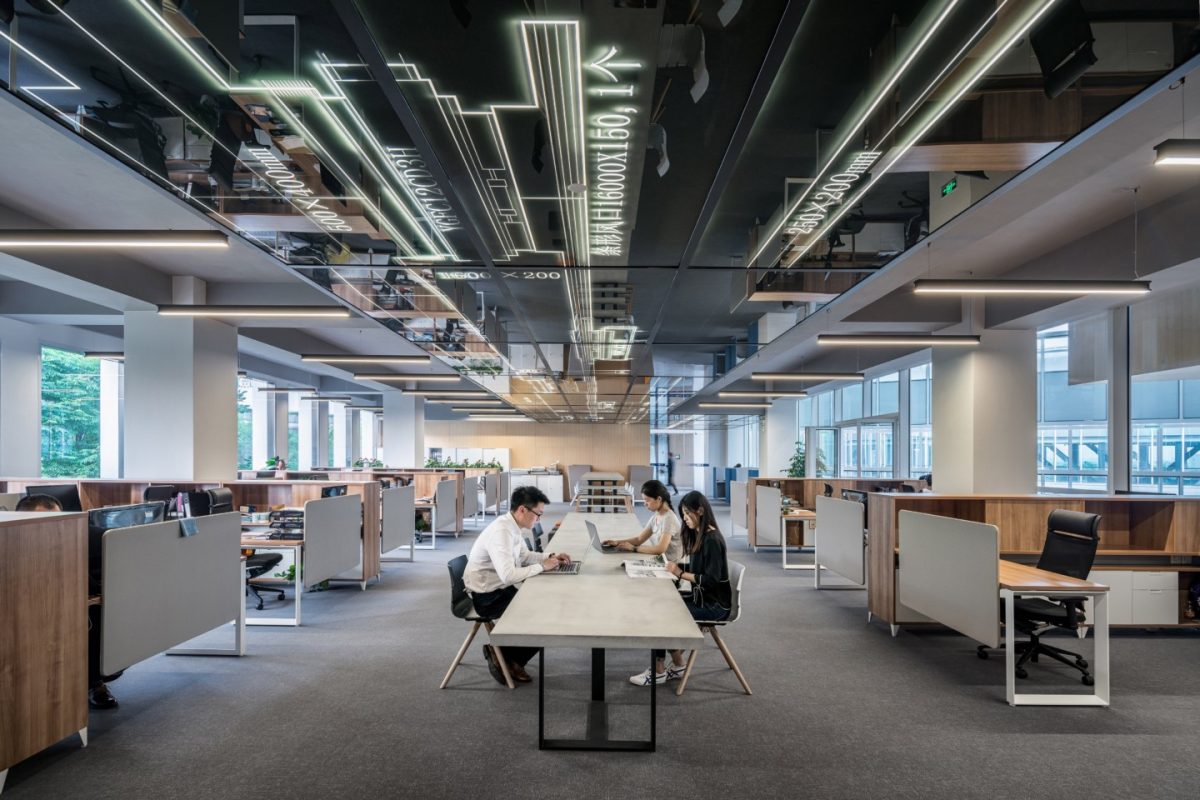 Two ladies sitting one side of table and one man opposite side of table in large open plan office