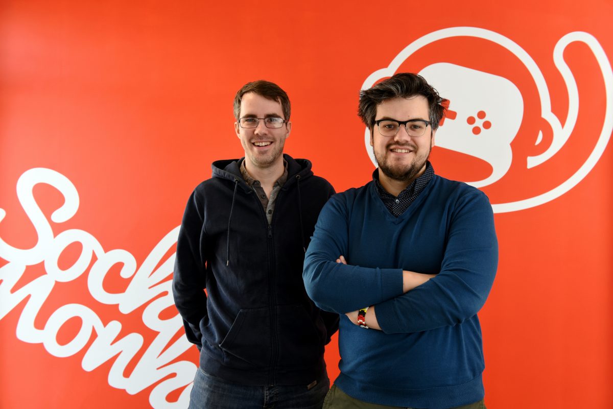 2 men smiling and stood in front of a Sock Monkey branded wall