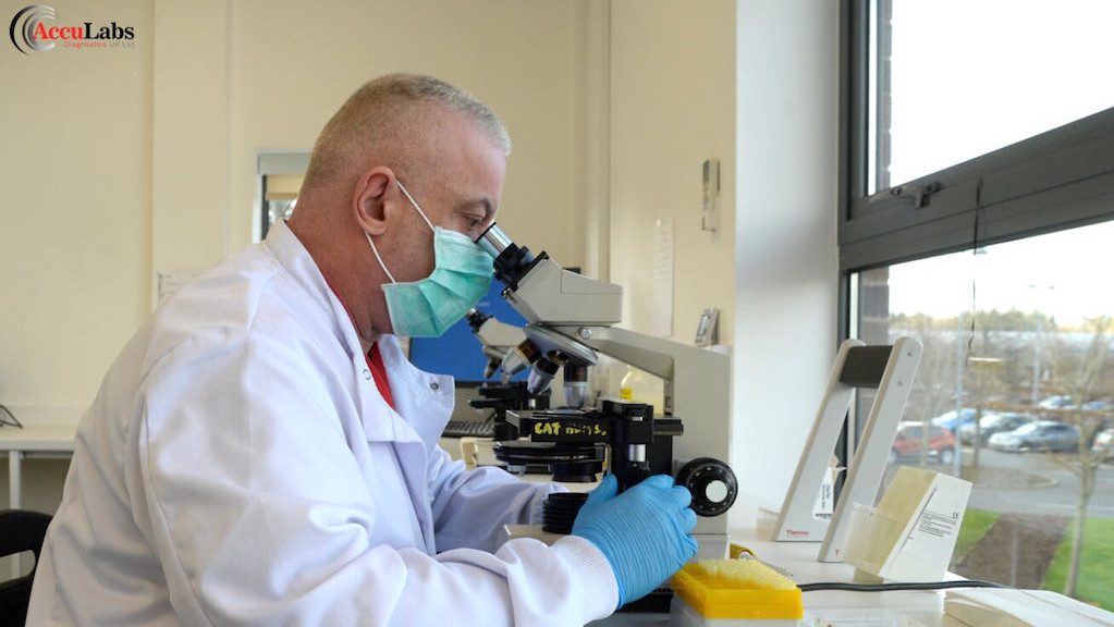 A man in a science lab wearing personal protective equipment looking into a microscope