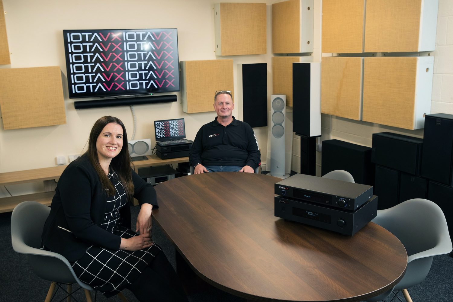 A man and a woman sat in a lota Enterprises sat in a meeting room with audio equipment