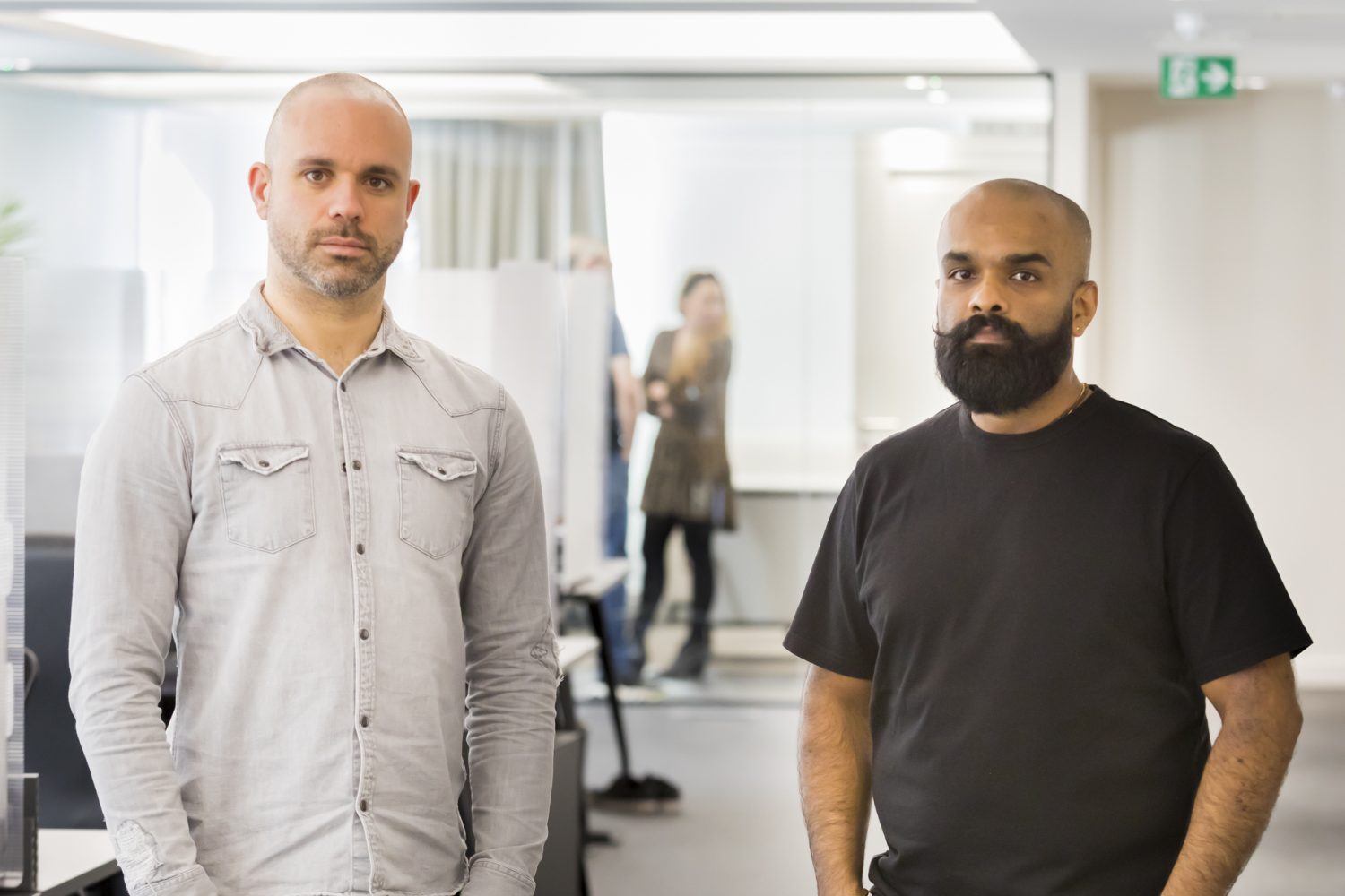 2 men stood in an office space with a meeting room in the background